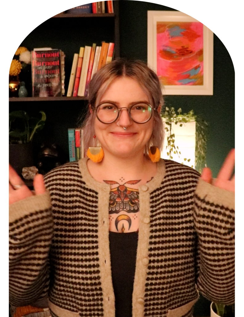 queer woman waves hello in front of bookcase