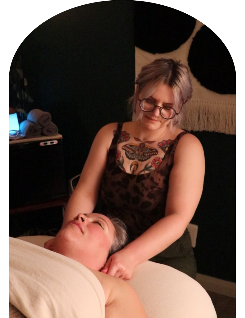 non-binary registered massage therapist in cozy room massages client's face
